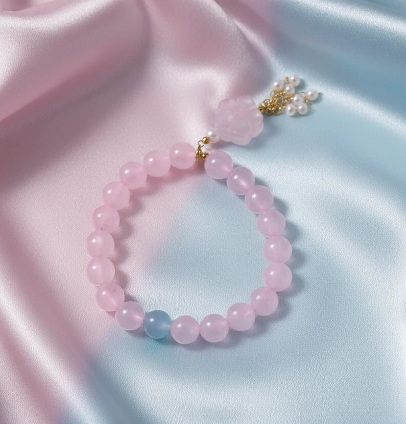 Stretchy beaded bracelet with pink rose quartz, blue aquamarine, carved floral pendant, and pearl tassel clasp.