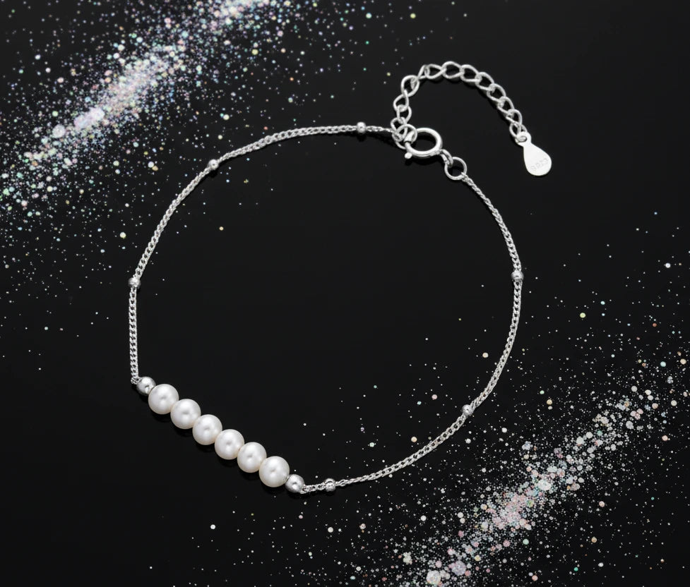 Delicate rhodium-plated silver chain bracelet with row of small baroque pearls centered on white background.