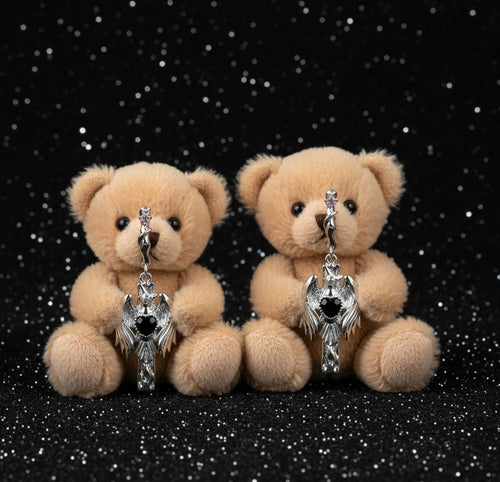 Silver drop earrings with twisted hoops and angel wings embracing black heart locket on white background.