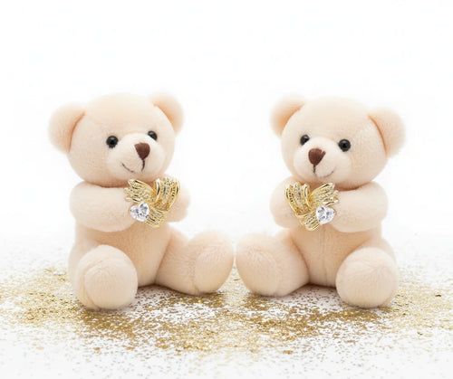 Pair of sculptural gold-plated wing stud earrings with zirconia stones on cream background, showing dimensional feather design