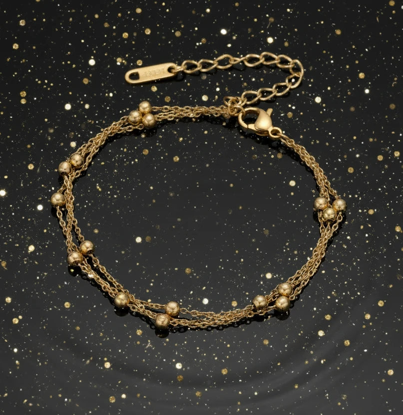 Three-strand gold-plated bracelet with clustered ball beads and adjustable clasp on cream background